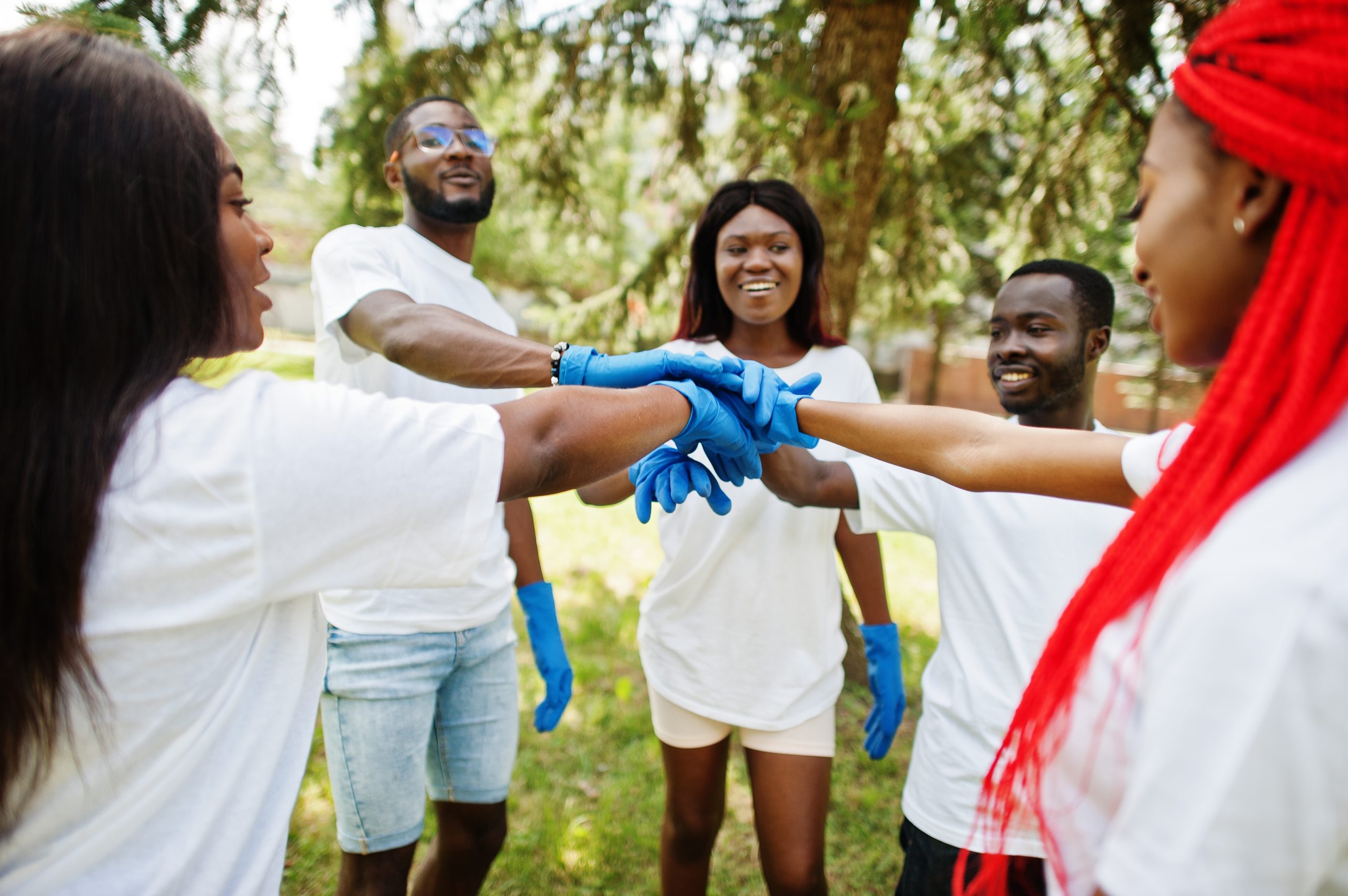 Group of happy african volunteers put hands in hands in park. Africa volunteering, charity, people and ecology concept.